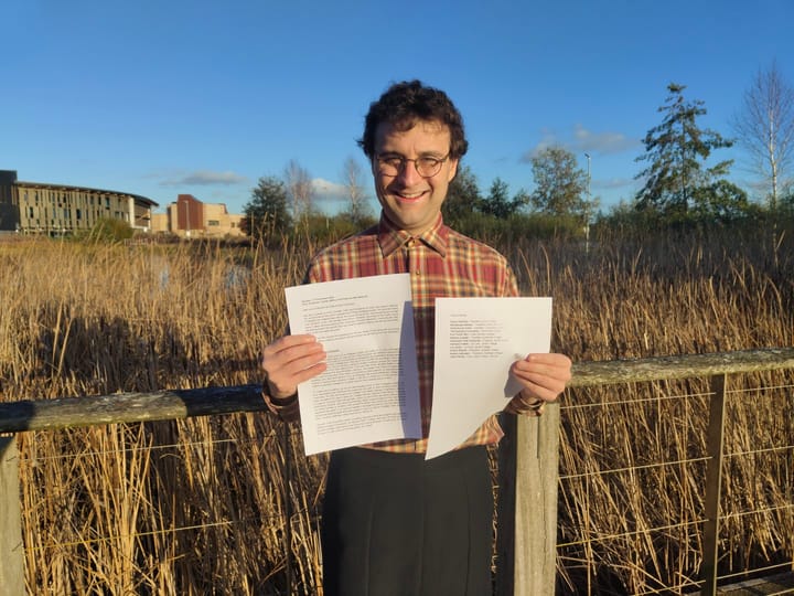 Simon Edwards holding letter in front of campus east lake.